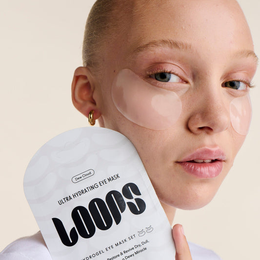 Woman holding a container of LOOPS ultra hydrating eye mask with patches on her face.