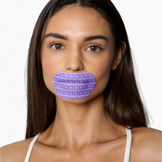 Woman with a purple patterned mouth tape lip mask over her mouth on a white background