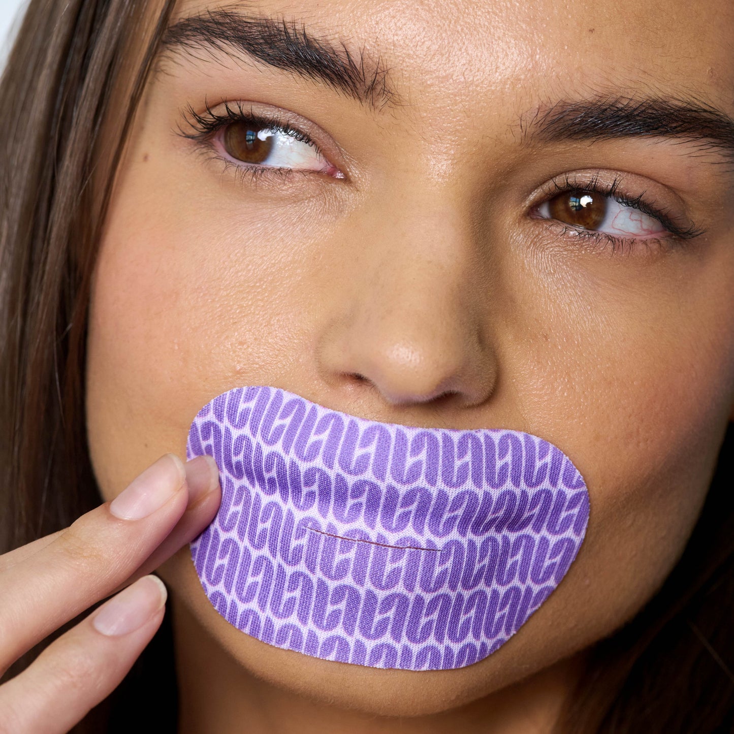 Close-up of a woman's face with a purple mouth tape mask over her mouth.