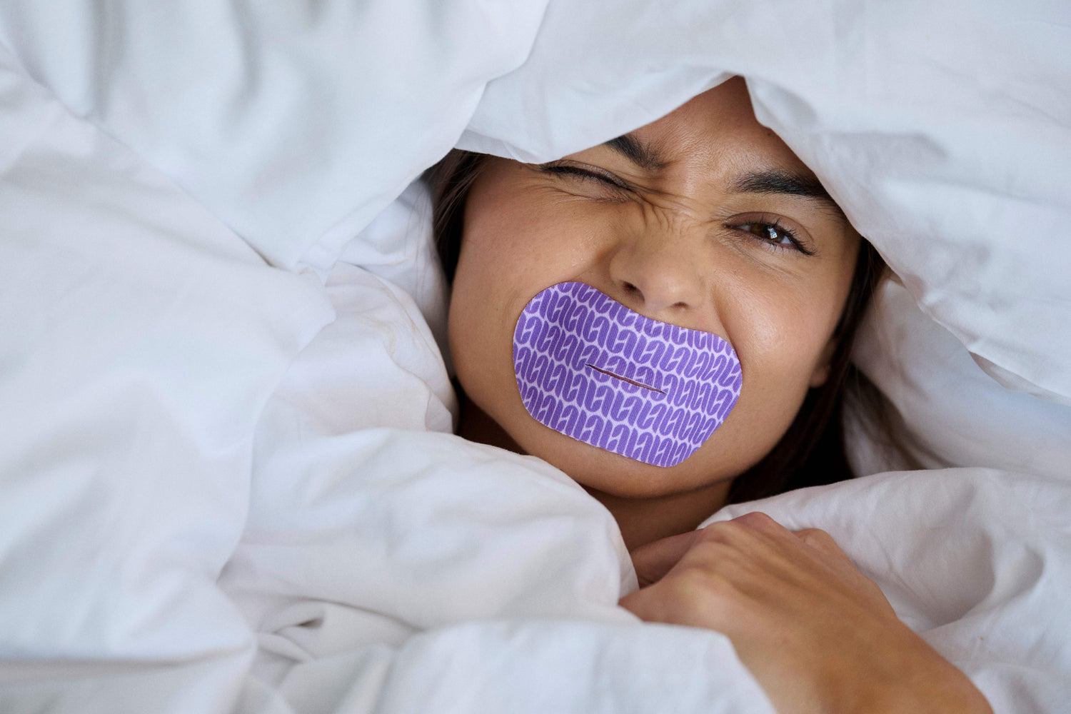 Person under white sheets with a purple 'LOOPS' mouth tape on their face