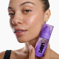 A close-up of a woman holding a purple bottle of Loops Night Shift Repairing Jelly Mist against a clean white background.