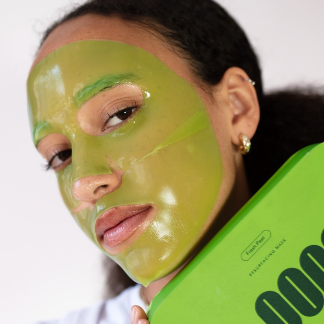 Female model facing forward with translucent green, 2-piece LOOPS Hydrogel face mask on while holding LOOPS carton pack.