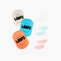 Three 'LOOPS' eye mask packages in different colors with eye masks on a white background.