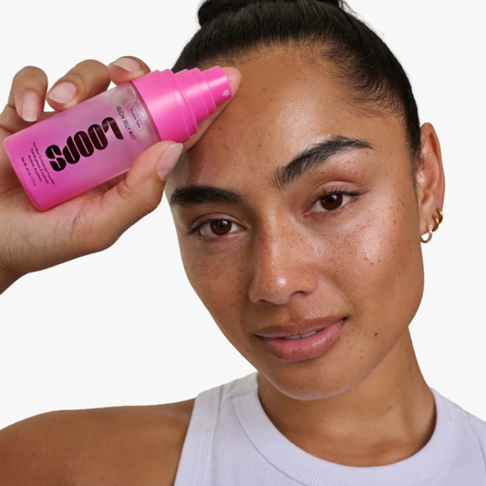 Person using a pink bottle labeled 'LOOPS' on their face against a white background