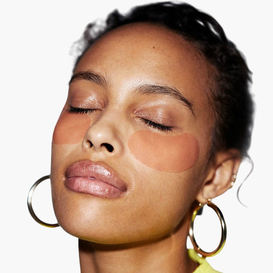 Close-up of a woman's face with orang eye masks on her undereye area against a white background