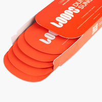 An orange cardboard box containing several matching orange circular face masks, photographed on a clean white background. The box lid has large white text reading 'LOOPS DUNE SUNCARE' and smaller text including '5 PERSONNEL FACE MASKS'.