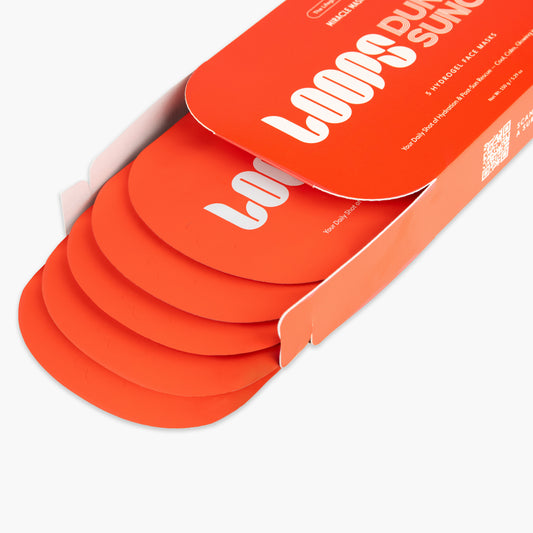 An orange cardboard box containing several matching orange circular face masks, photographed on a clean white background. The box lid has large white text reading 'LOOPS DUNE SUNCARE' and smaller text including '5 PERSONNEL FACE MASKS'.