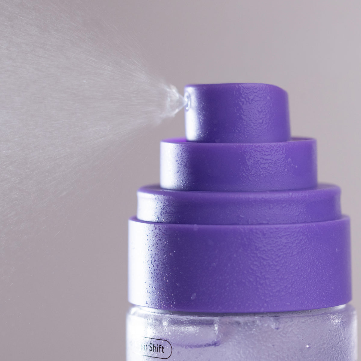 Close-up of a purple spray bottle nozzle releasing a fine mist against a soft gray background.