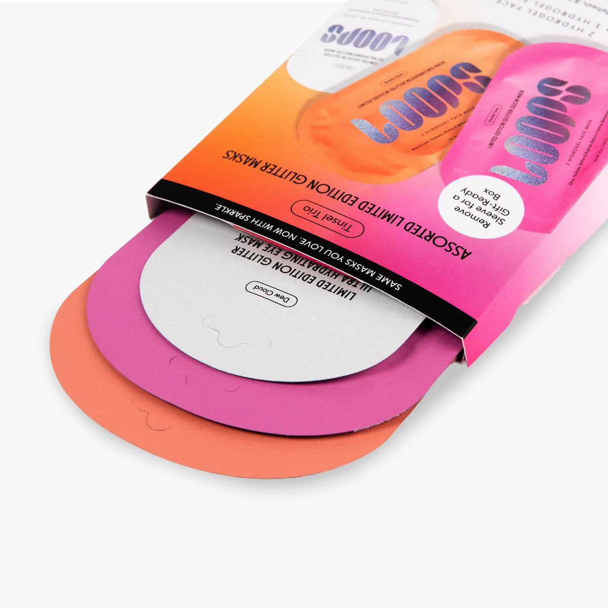 A close-up of a packaged sheet mask set on a clean white background. The product includes three oval-shaped paper masks in orange, pink, and white, partially pulled from a bright pink and orange cardboard sleeve with black text and a white circular sticker.