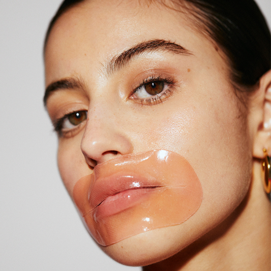 Female model facing forward with orange,  LOOPS Hydrogel lip mask on.